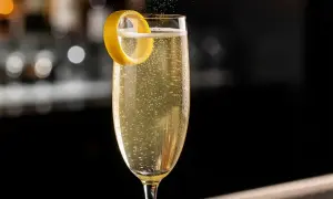 Ett glas French 75 med bubblor och en citronskal.