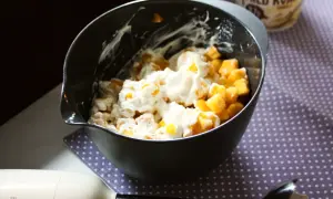 En skål med fruktbitar och krämig kvarg, redo att bli en härlig kvarg glass. En stavmixer ligger bredvid.