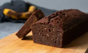 En saftig banankaka i sockerkaksform, med en skiva upplagd. En övermogen banan ligger i bakgrunden.