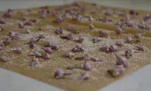 Små lila syrenblommor strös med socker på bakplåtspapper, redo att bli kanderade syrenblommor.