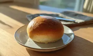 En gyllene, luftig semla på en tallrik, redo att fyllas med grädde och mandelmassa. Solen lyser in genom fönstret.