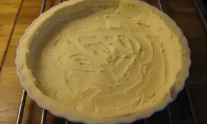 En ljusgul, krämig glutenfri pajdeg i en vit pajform, redo att fyllas.