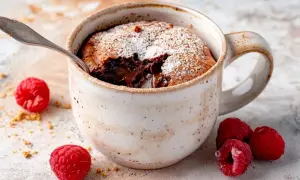 En härlig kladdkaka i mugg med smält choklad, pudrad med florsocker och omgiven av färska hallon.