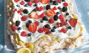 En stor pavlova med lemoncurd, toppad med vispgrädde och färska bär som jordgubbar, hallon, blåbär och vinbär.