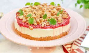 En läcker rabarber cheesecake med smulig topping och myntablad, serverad på ett rosa tårtfat.