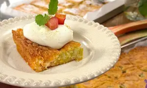 En bit saftig rabarberkaka i långpanna, toppad med fluffig grädde och färska rabarberbitar. Perfekt till fikat!