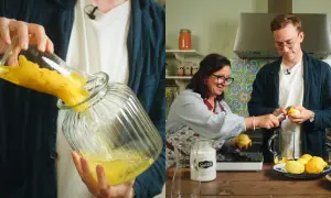 Två personer förbereder egen limoncello i ett kök. En häller citroner i en glasburk, medan den andra skalar citroner.