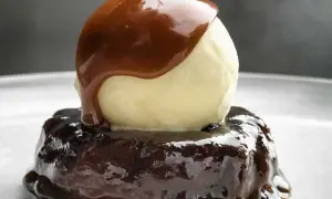 En läcker sticky toffee pudding med en kula vaniljglass och varm kolasås som rinner över.