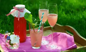 En flaska rabarberdryck och två glas med rabarberdrink med prosecco står på en bricka i gräset.