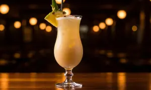 En krämig alkoholfri pina colada med ananasskiva och blad som dekoration, serverad i ett elegant glas på en träyta.
