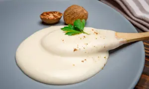 Krämig bechamelsås på en tallrik med muskotnötter och persilja. Perfekt för ditt bechamelsås recept.