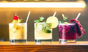 Tre färgglada alkoholfria drinkar med frukt och mynta på en träbar.