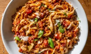 En skål med tagliatelle täckt av en mustig vegetarisk pastasås med linser, tomater och basilika, toppad med parmesan.