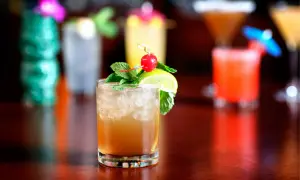 En Mai Thai-drink med is, mynta, lime och körsbär. I bakgrunden syns fler drinkar och en grön tiki-mugg.