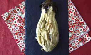 En ugnsbakad aubergine, mjuk och saftig, serveras på en svart skifferplatta.