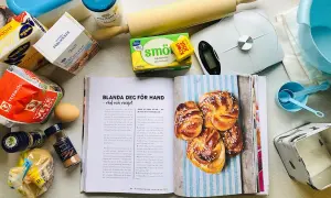 Här finns allt för ett lyckat kanelbullar recept: mjöl, jäst, smör, socker, kardemumma och kanel. En öppen bok visar hur man gör.