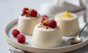 Tre krämiga panna cotta-desserter med hallon och citronskal på en tallrik.