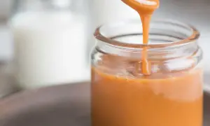 En sked häller krämig kolasås i en glasburk. Perfekt för ditt kolasås recept!