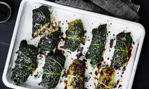 Kåldolmar recept: Väl tillagade kåldolmar på en plåt, glaserade och toppade med sesamfrön och örter.