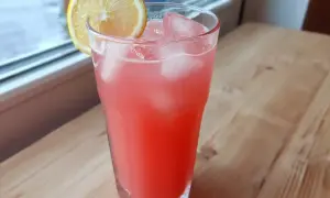 Ett glas rosa rabarberlemonad med is och en citronskiva, redo att avnjutas.