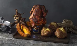 En saftig ölburkskyckling med majskolvar och bakpotatis på ett fat.