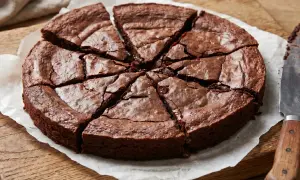 En saftig glutenfri kladdkaka, uppskuren i åtta bitar på bakplåtspapper. En kniv ligger bredvid.