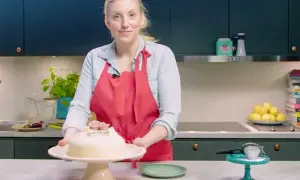 Kvinna med röd förkläde presenterar en marsipantårta. Ett perfekt marsipan recept för firande.