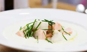 En krämig soppa med bitar av confiterad lax och vit fisk, toppad med färsk gräslök.