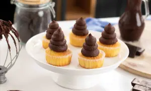 Fem cupcakes med chokladganache, perfekt för ett enkelt ganache recept. Ingredienser för bakning syns i bakgrunden.