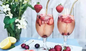Två glas med drink med gin och prosecco, fyllda med is, jordgubbar och körsbär. Garnerade med jordgubbar och serverade med citroner och blommor.