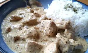 En krämig sås till kyckling och ris, med bitar av kyckling i en len sås. Riset är toppat med lite grön krydda.