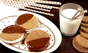 S'mores i ugn: tre chokladöverdragna kex med marshmallowfyllning på en prickig tallrik, bredvid ett glas mjölk och fler kex.