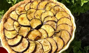 En paj med gyllene, stekt aubergine och rosmarin, vackert arrangerad i en ljusgul form.