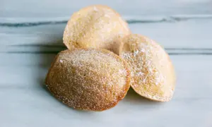 Tre gyllene madeleines, pudrade med florsocker, redo att avnjutas. Ett enkelt och gott madeleine recept.