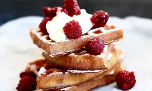 En stapel gyllene belgiska våfflor toppade med vispad grädde och färska hallon, pudrade med florsocker. En härlig frukost eller dessert.