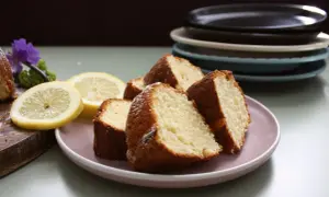 Skivor av saftig citron sockerkaka på en ljusrosa tallrik, med citronskivor och en lila blomma som dekoration.