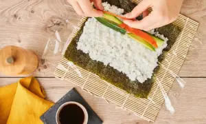 Händer lägger lax och gurka på ris för ett sushi recept.