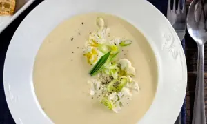 Krämig potatis och blomkålssoppa med garnering av blomkål, salladslök och peppar. Serveras med en bit rostat bröd.