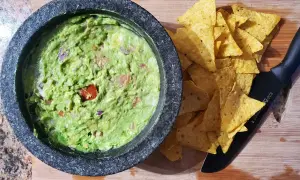 Närbild på en skål med hemgjord guacamole, perfekt för ett enkelt guacamole recept. Tortillachips och en kniv ligger bredvid.