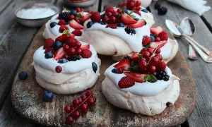 Små pavlova med grädde och färska bär som jordgubbar, hallon, blåbär och vinbär. En härlig sommardessert.