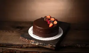 En lyxig fransk chokladtårta med färska bär och chokladdekorationer, serverad på en rustik träbricka.