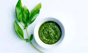 En skål med grön pesto bredvid färska basilikablad. Perfekt för ett enkelt pesto recept.