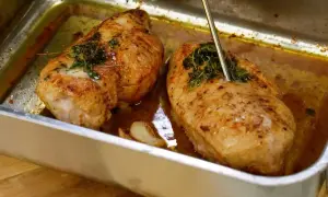 Två saftiga kycklinglårfiléer i en ugnsform, kryddade med örter och vitlök. En termometer mäter temperaturen för perfekt grillad kyckling.