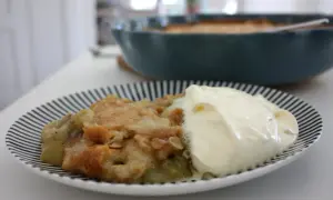 En portion rabarberpaj med kardemumma och en klick grädde på en randig tallrik.