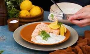 En bit lax med citron och dill, toppad med en krämig klassisk romsås. En gaffel med sås och rom lyfts från skålen.