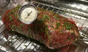 En fransyska i ugn, förberedd för låg temperaturstekning med örtkryddor och en köttermometer.