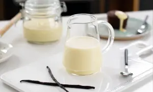 En liten kanna med krämig vaniljsås, perfekt till efterrätt. Två vaniljstänger ligger bredvid.