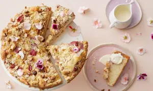 En härlig glutenfri rabarberkaka med havregryn och nötter, dekorerad med blommor. En bit serveras med grädde.
