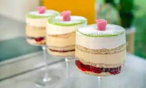 Tre vackra prinsesstårtor i glas, lager av sockerkaka, grädde och sylt, toppade med grön marsipan och en rosa ros.
