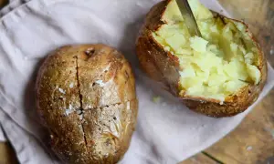 Två fluffiga bakade potatisar i airfryer, en med en kniv som skär i den mjuka insidan. Perfekt för en snabb och god måltid.